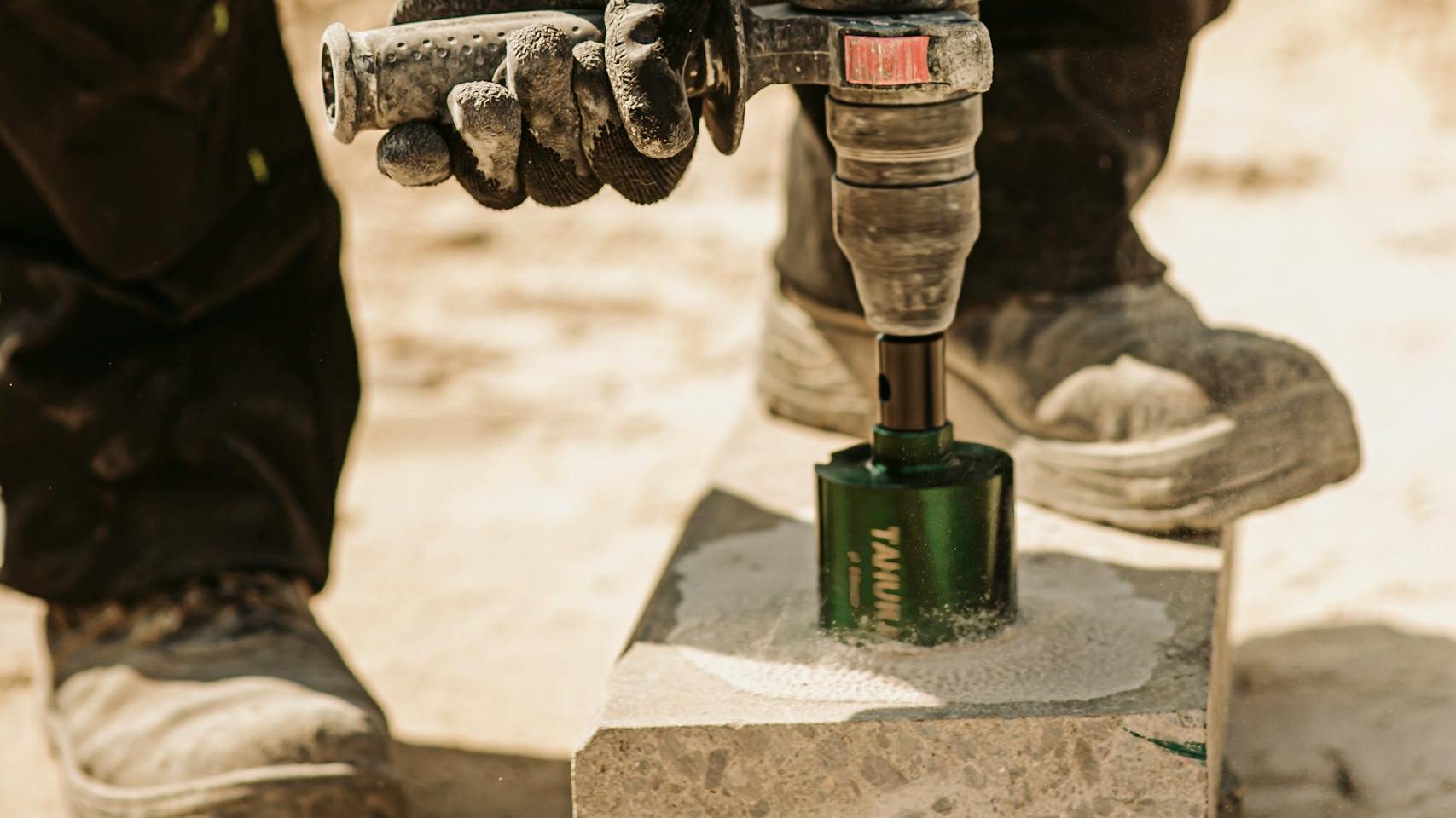 Close-up of a construction worker using a power tool to drill concrete outdoors on a sunny day.